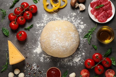 Flat lay composition with dough and fresh ingredients for pizza on grey table