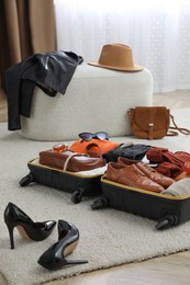 Photo of Open suitcase with folded clothes, accessories and shoes on floor indoors