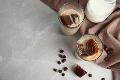 Photo of Glasses of milk with coffee ice cubes on grey table, top view. Space for text