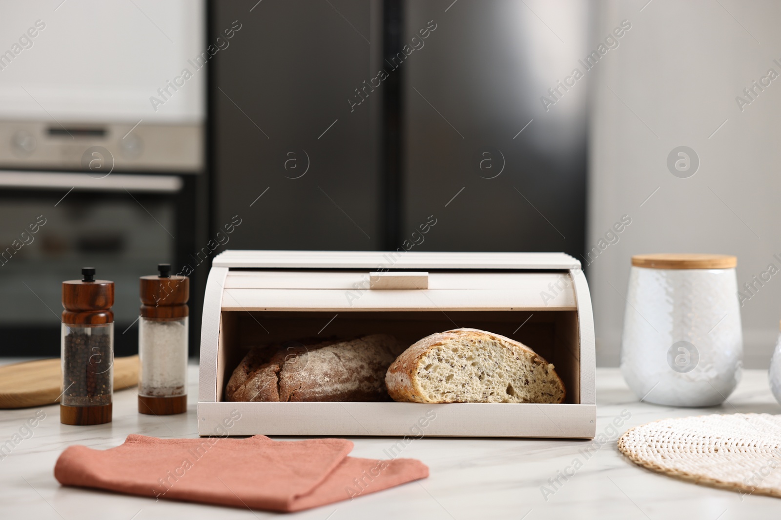 Photo of Wooden bread basket with freshly baked loaves on white marble table in kitchen