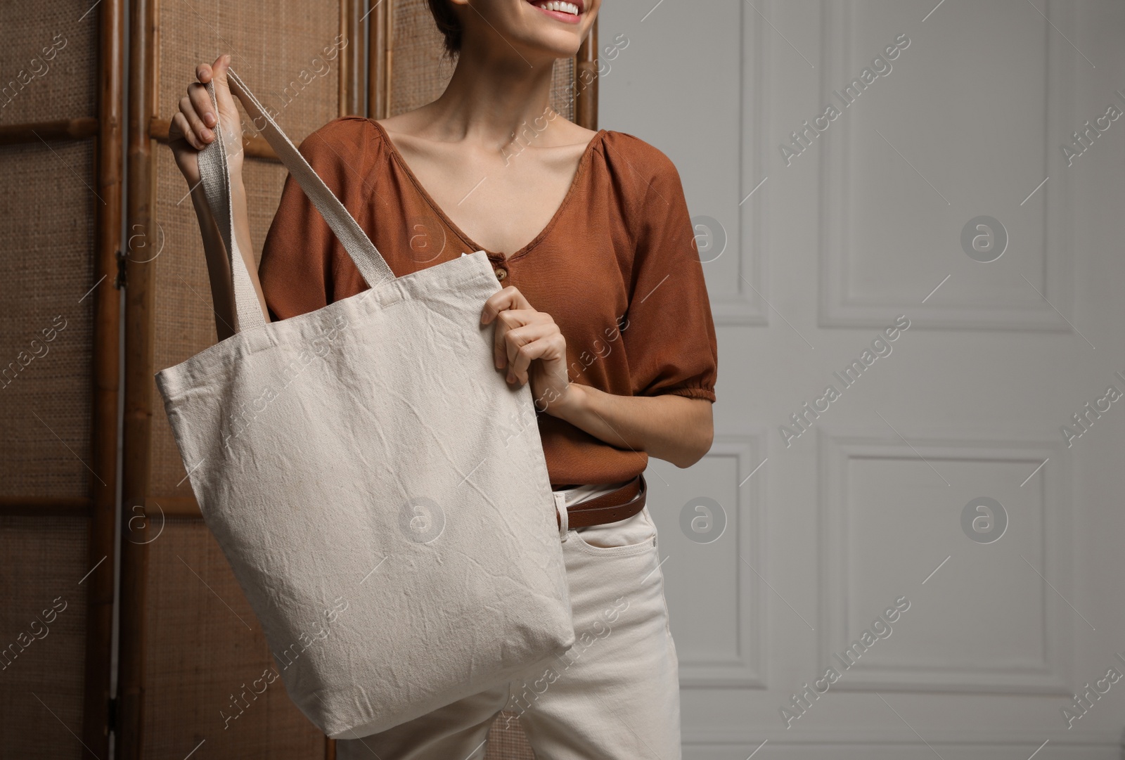 Photo of Happy young woman with blank eco friendly bag indoors, closeup. Space for text