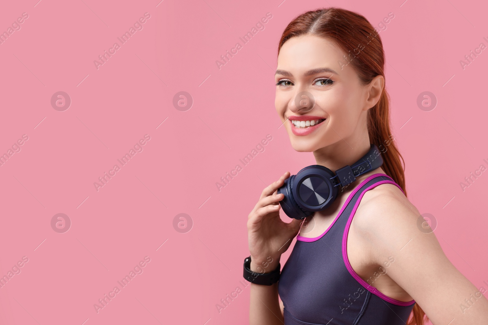 Photo of Woman in sportswear and headphones on pink background, space for text