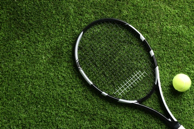 Photo of Tennis racket and ball on green grass, flat lay. Space for text