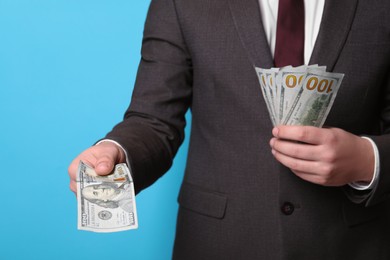 Man holding money on light blue background, closeup. Currency exchange