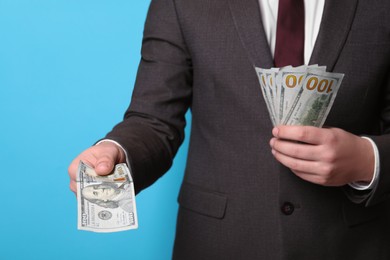 Photo of Man holding money on light blue background, closeup. Currency exchange