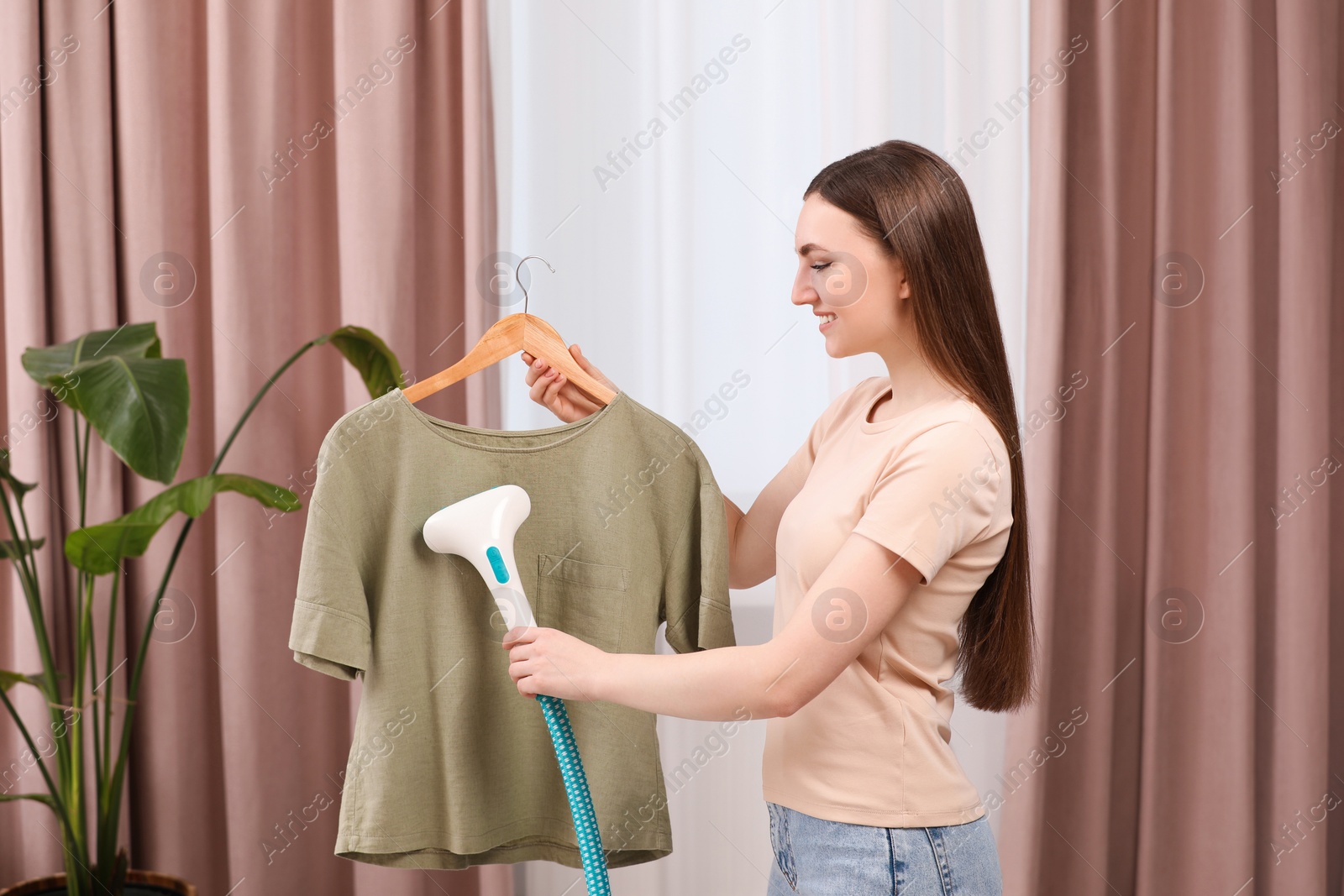 Photo of Woman steaming shirt on hanger at home