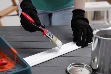 Photo of Woman painting plank with white dye at black wooden table indoors, closeup