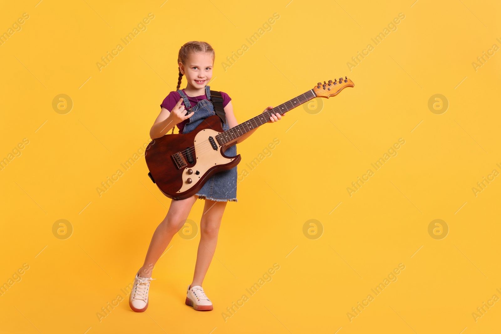 Photo of Cute girl with electric guitar on orange background