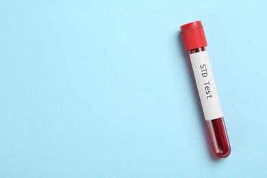Photo of Tube with blood sample and label STD Test on light blue background, top view. Space for text