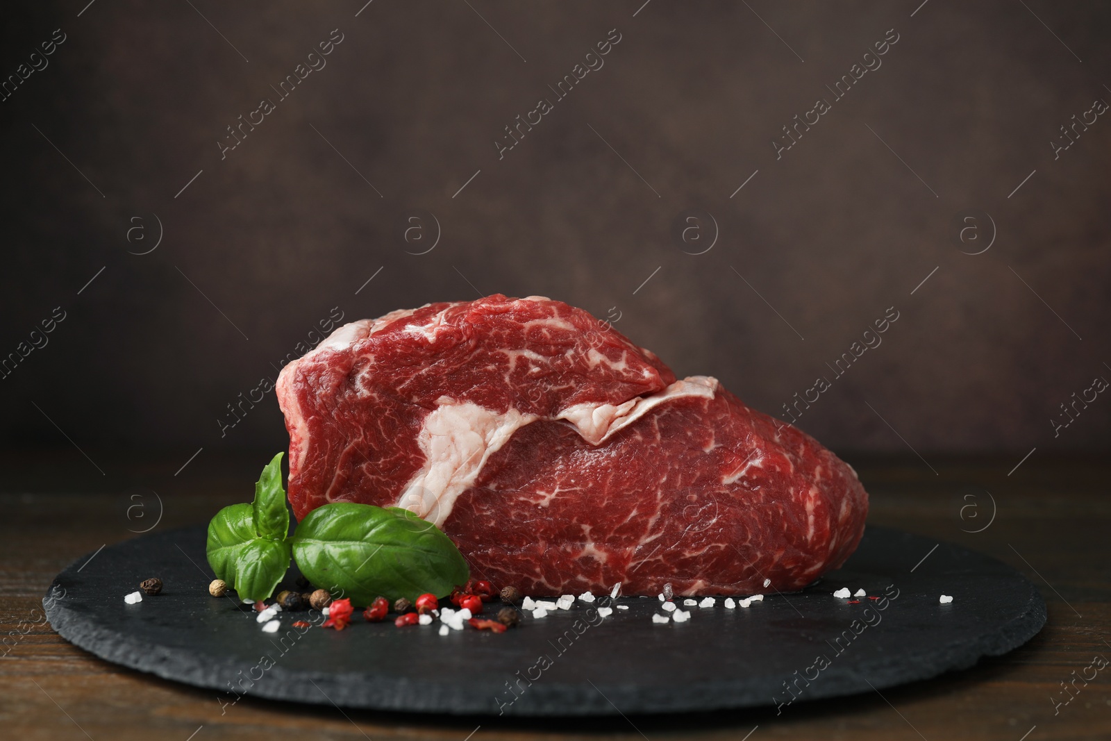 Photo of Fresh raw cut beef, spices and basil leaves on wooden table