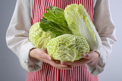 Photo of Woman holding different types of cabbages on light grey background, closeup