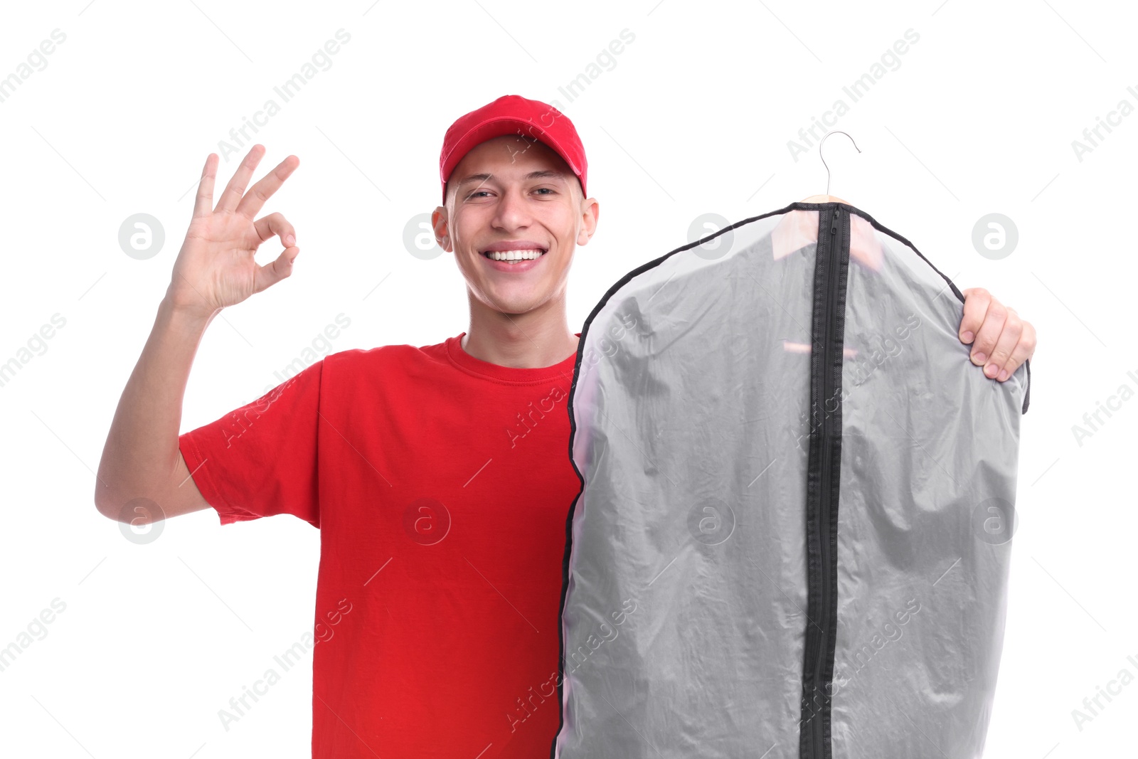 Photo of Dry-cleaning delivery. Happy courier holding garment cover with clothes and showing OK gesture on white background