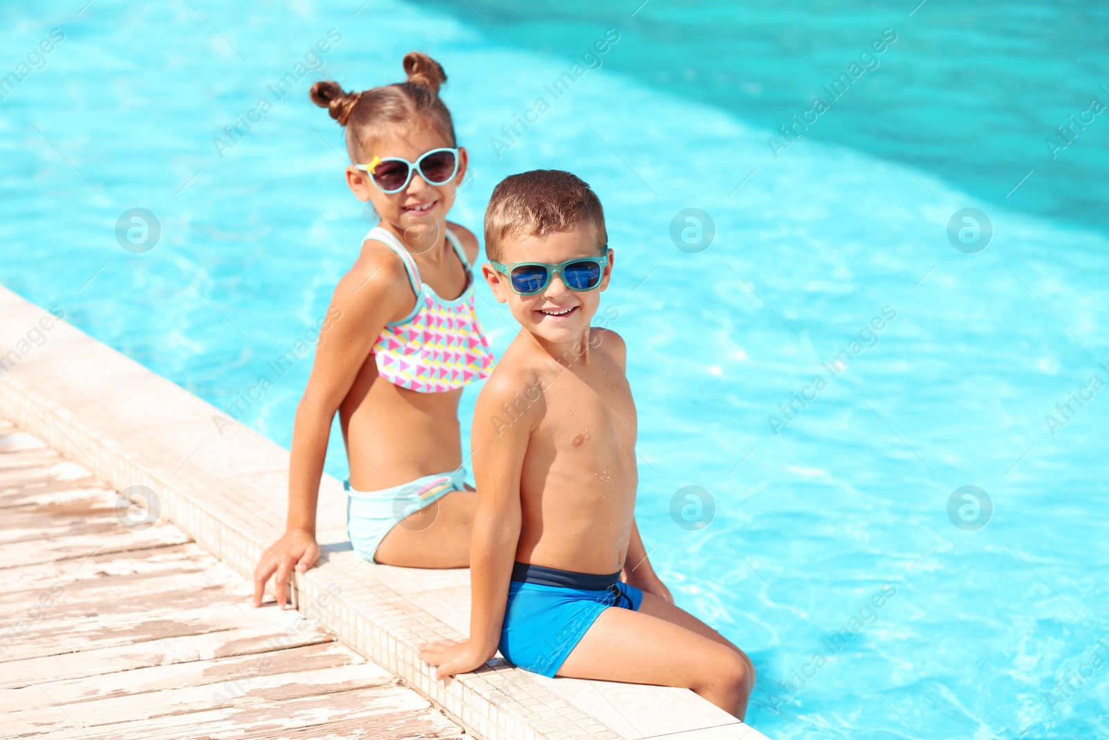 Photo of Cute little children sitting near swimming pool