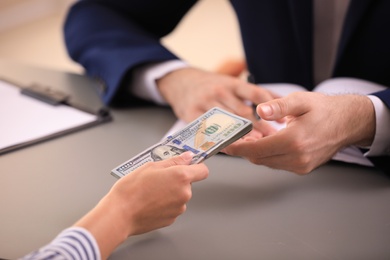 Photo of Young woman giving dollar bills to businessman in office, closeup