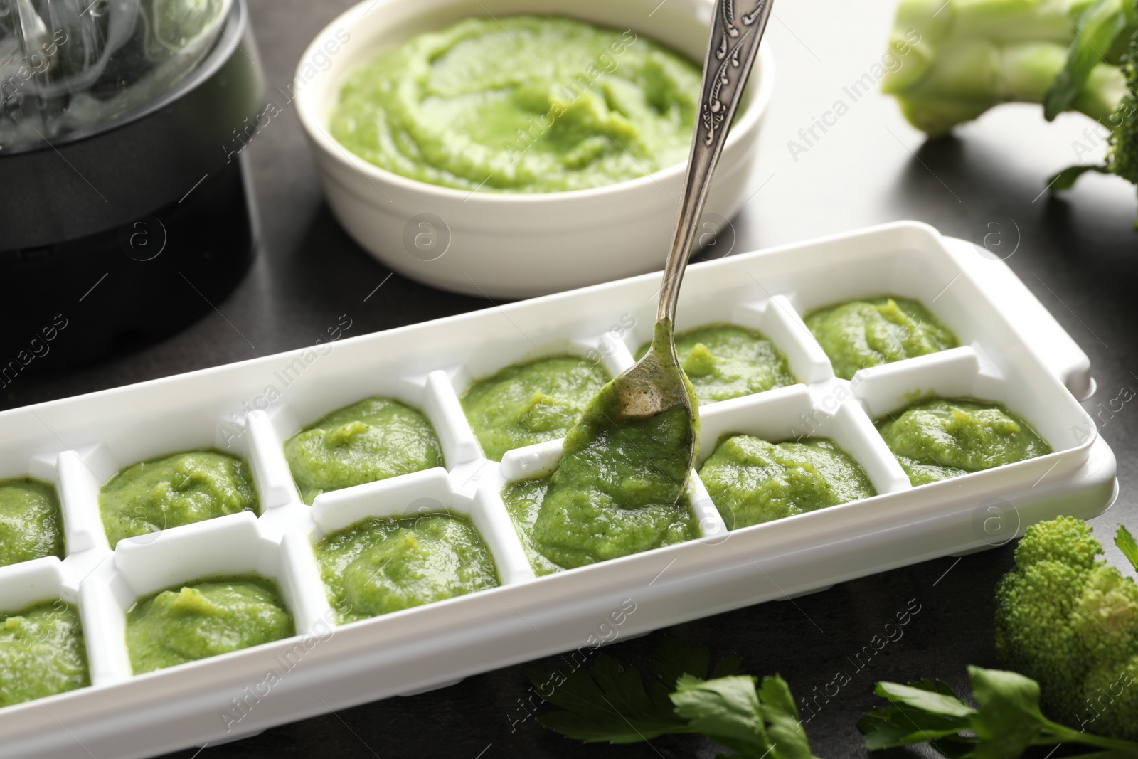 Photo of Putting puree with spoon into ice cube tray on table, closeup. Ready for freezing