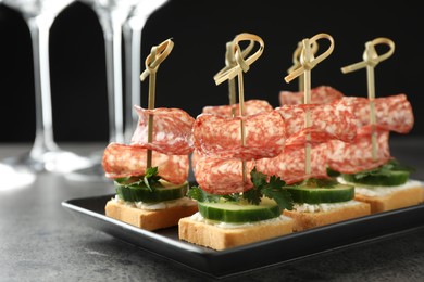 Photo of Tasty canapes with salami, cucumber and cream cheese on grey table, closeup