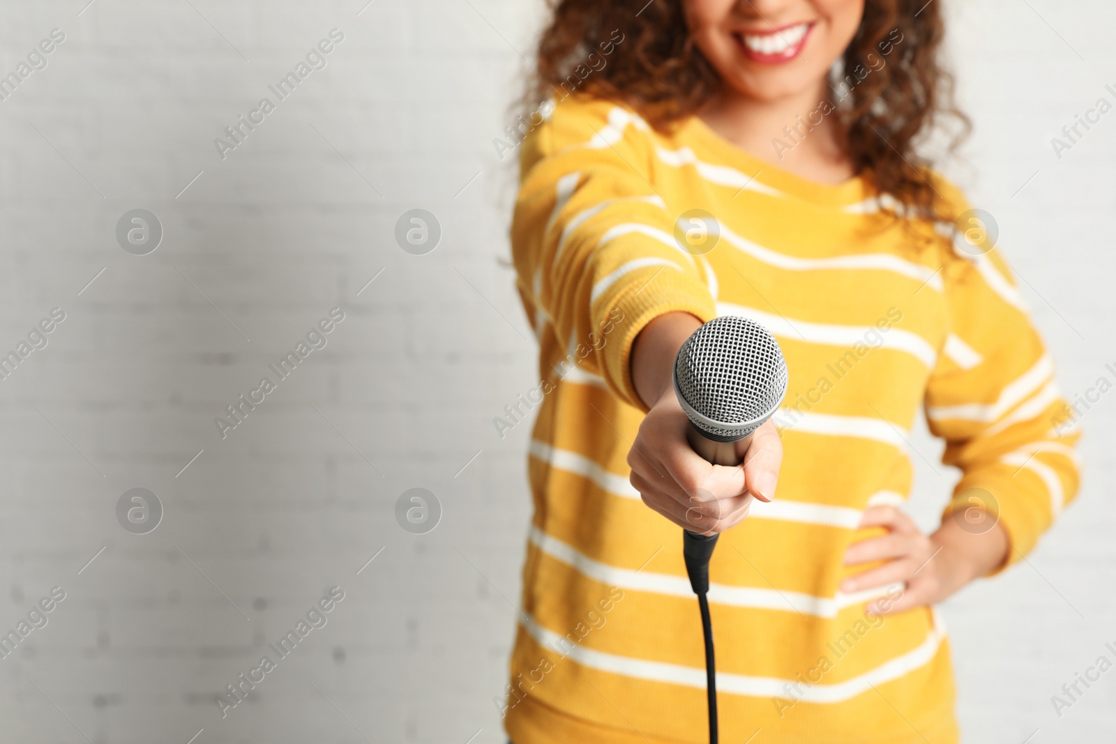 Photo of Curly African-American woman in sweater holding microphone near brick wall, closeup with space for text