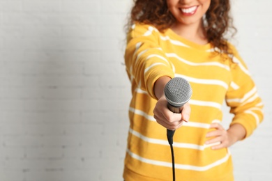 Photo of Curly African-American woman in sweater holding microphone near brick wall, closeup with space for text