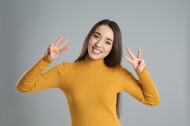 Woman in yellow turtleneck sweater showing number six with her hands on grey background