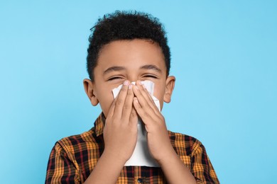 Photo of African-American boy blowing nose in tissue on turquoise background. Cold symptoms