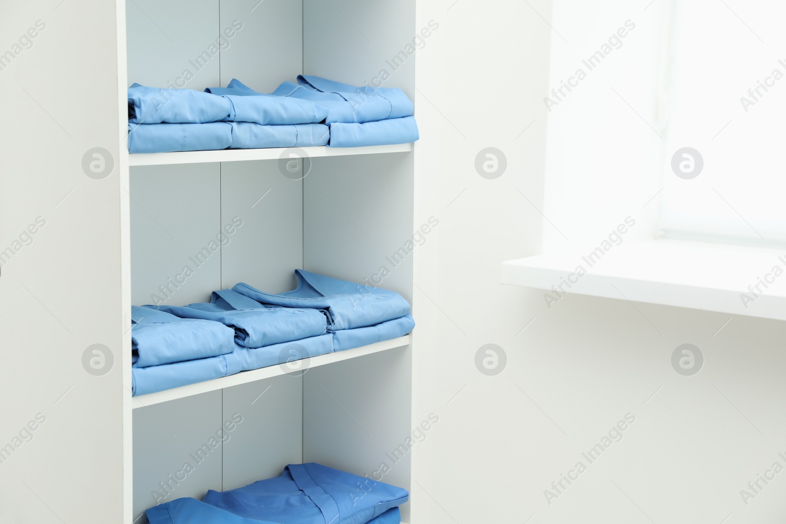 Photo of Light blue medical uniforms on white rack indoors, space for text