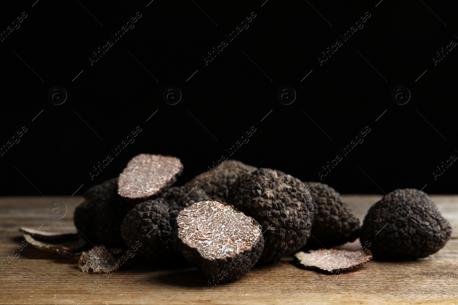 Photo of Whole and cut truffles on wooden table against black background