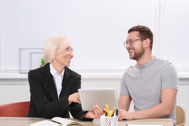 Photo of Happy boss with tablet and employee discussing work issues at wooden table in office