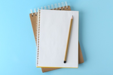 Photo of Notebooks with pencil on light blue background, top view