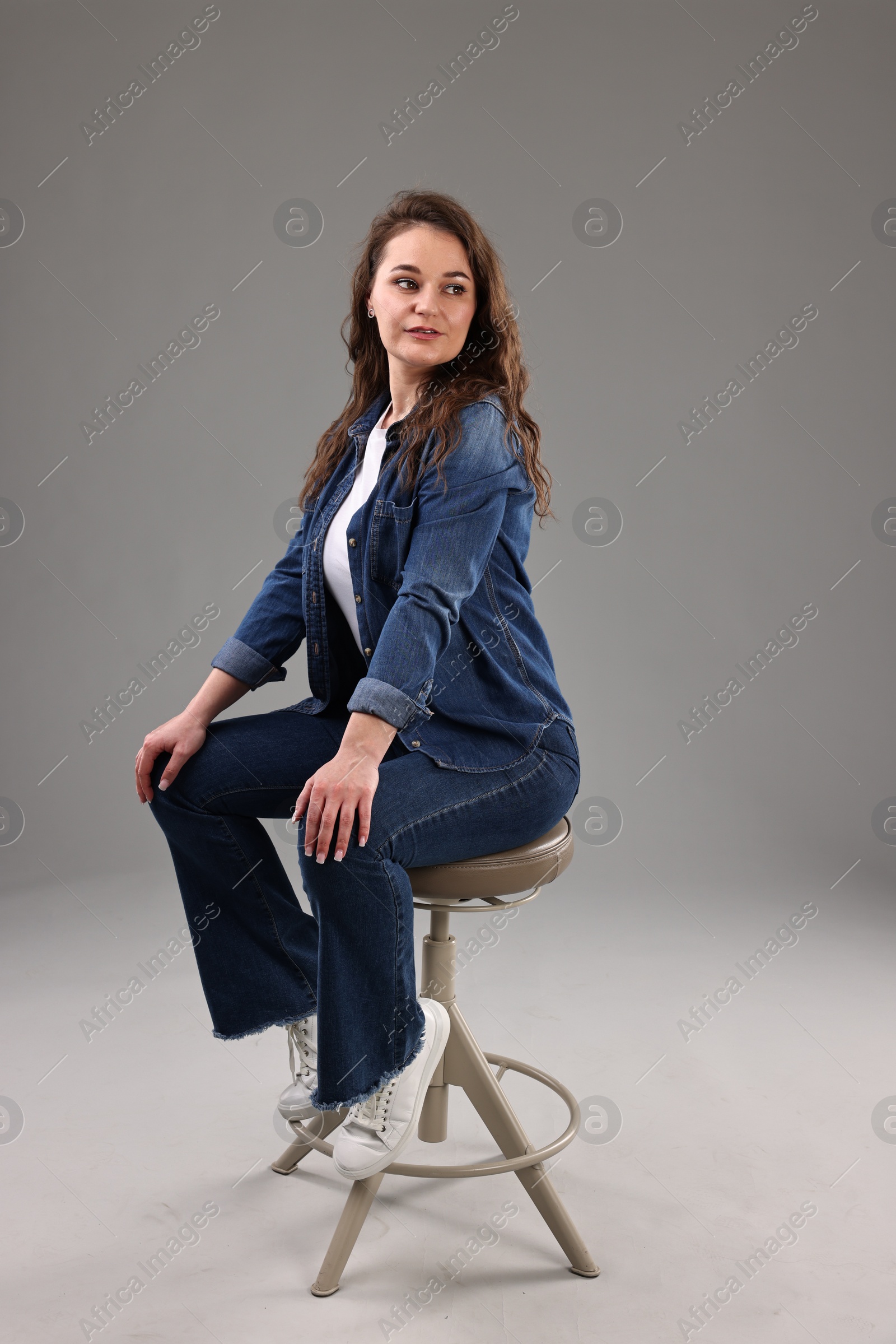 Photo of Portrait of beautiful young woman sitting on chair against grey background