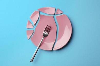 Photo of Pieces of broken ceramic plate and fork on light blue background, flat lay