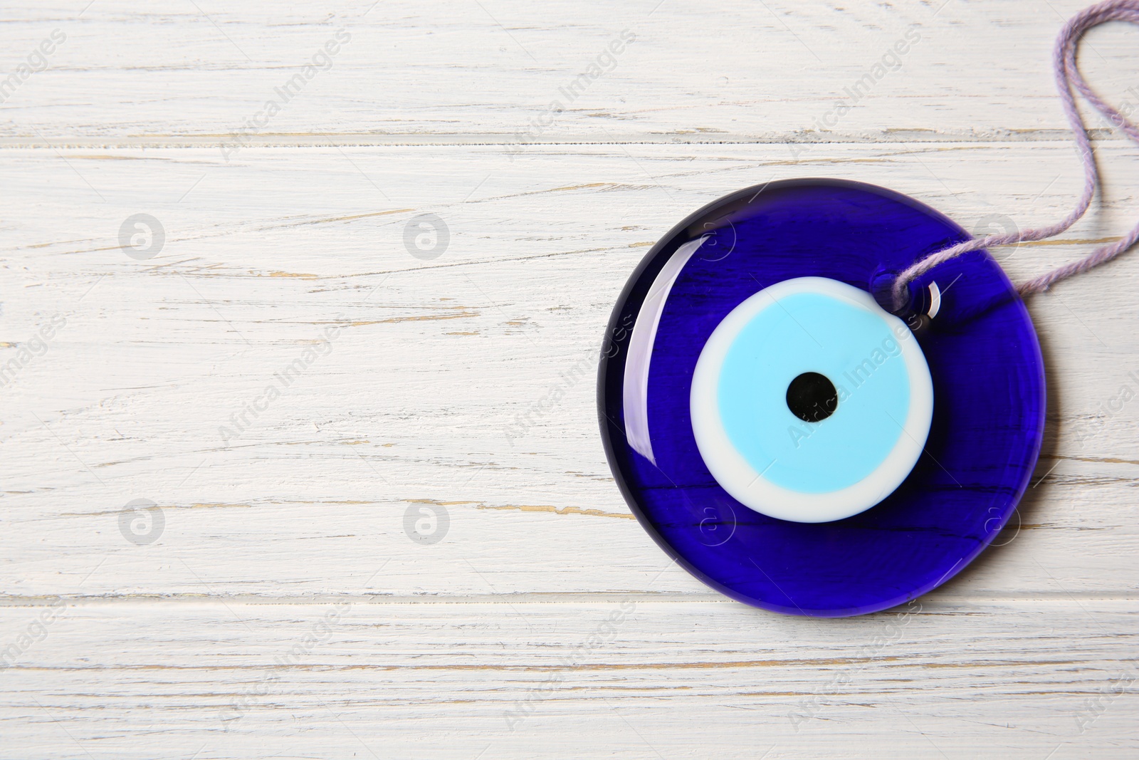 Photo of Evil eye amulet on white wooden table, top view. Space for text