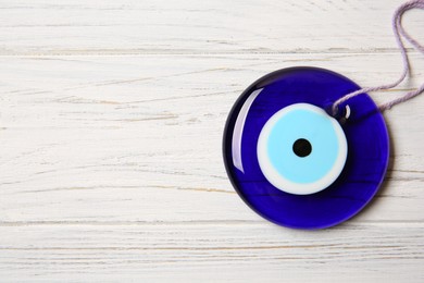 Photo of Evil eye amulet on white wooden table, top view. Space for text