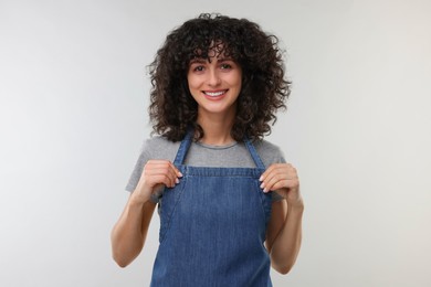 Happy woman wearing kitchen apron on light grey background. Mockup for design
