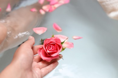 Woman holding rose flower while taking bath, closeup. Romantic atmosphere