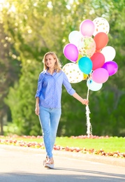 Young woman with colorful balloons in park on sunny day