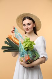 Photo of Woman with string bag of fresh vegetables and baguette on beige background