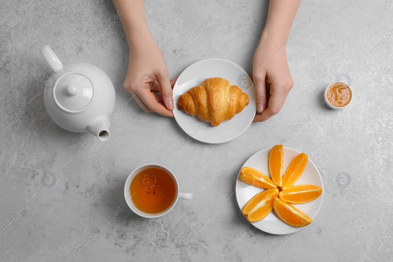 Photo of Young woman having breakfast with tasty croissant and cup of tea at table, top view