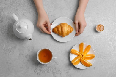 Young woman having breakfast with tasty croissant and cup of tea at table, top view