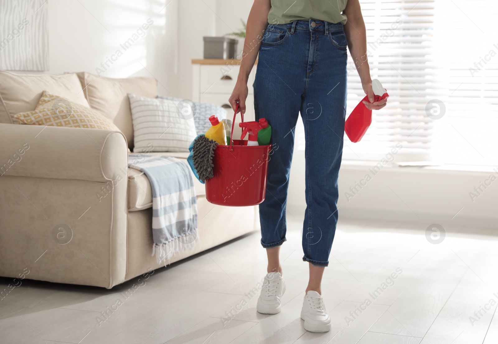 Photo of Woman holding bucket with different cleaning supplies at home, closeup