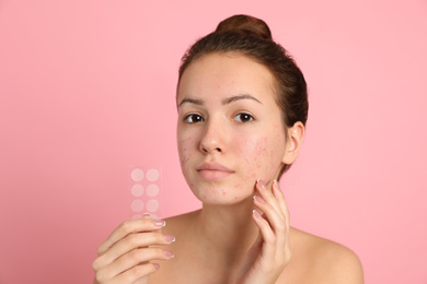 Photo of Teen girl holding acne healing patches on light pink background