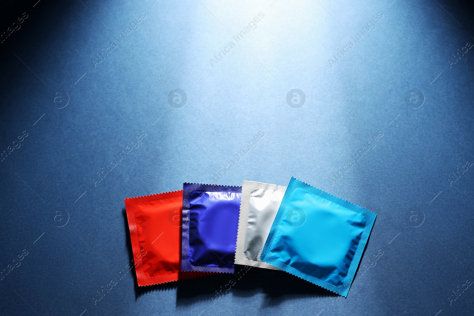 Photo of Packaged condoms on blue background, top view with space for text. Safe sex