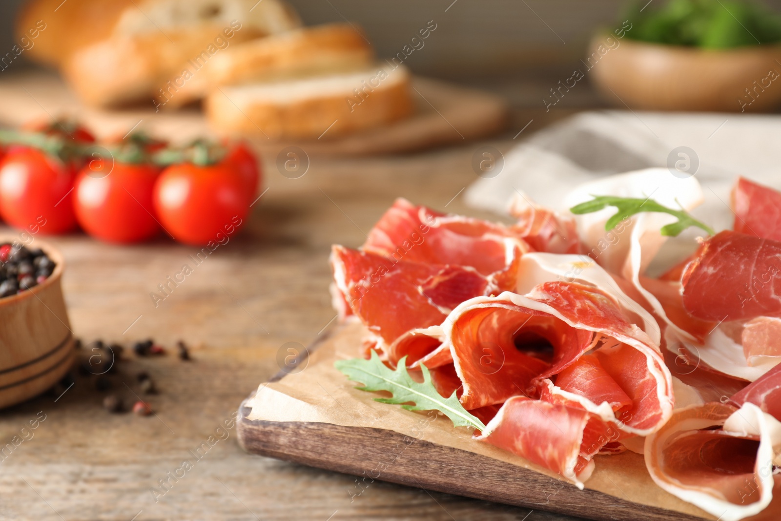 Photo of Pile of tasty prosciutto on wooden table, closeup