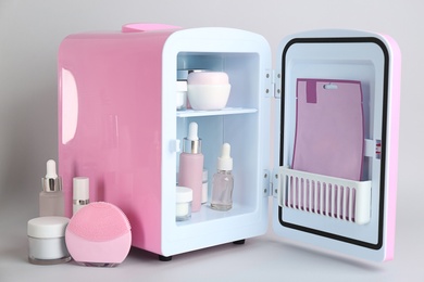 Photo of Open cosmetic refrigerator and skin care products on light background