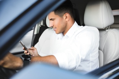 Photo of Handsome man using smartphone while driving his modern car