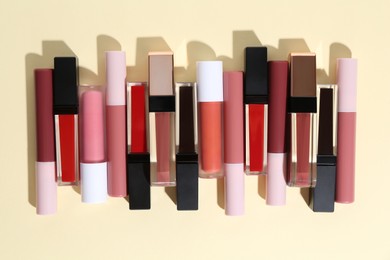 Photo of Different lip glosses on pale yellow background, flat lay