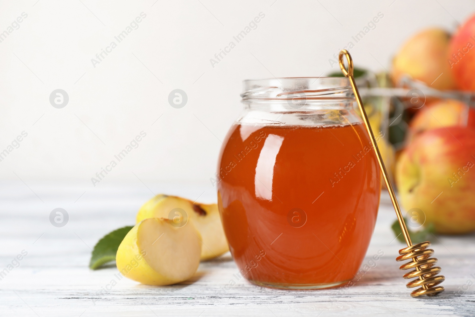 Photo of Jar of honey, apples and dipper on wooden table