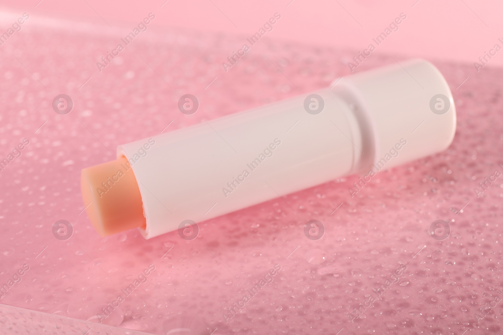 Photo of Lip balm and water drops on pink glass surface, closeup