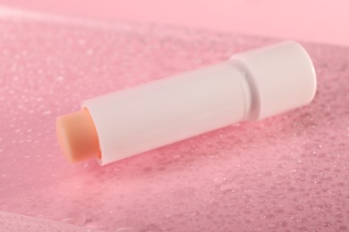 Lip balm and water drops on pink glass surface, closeup