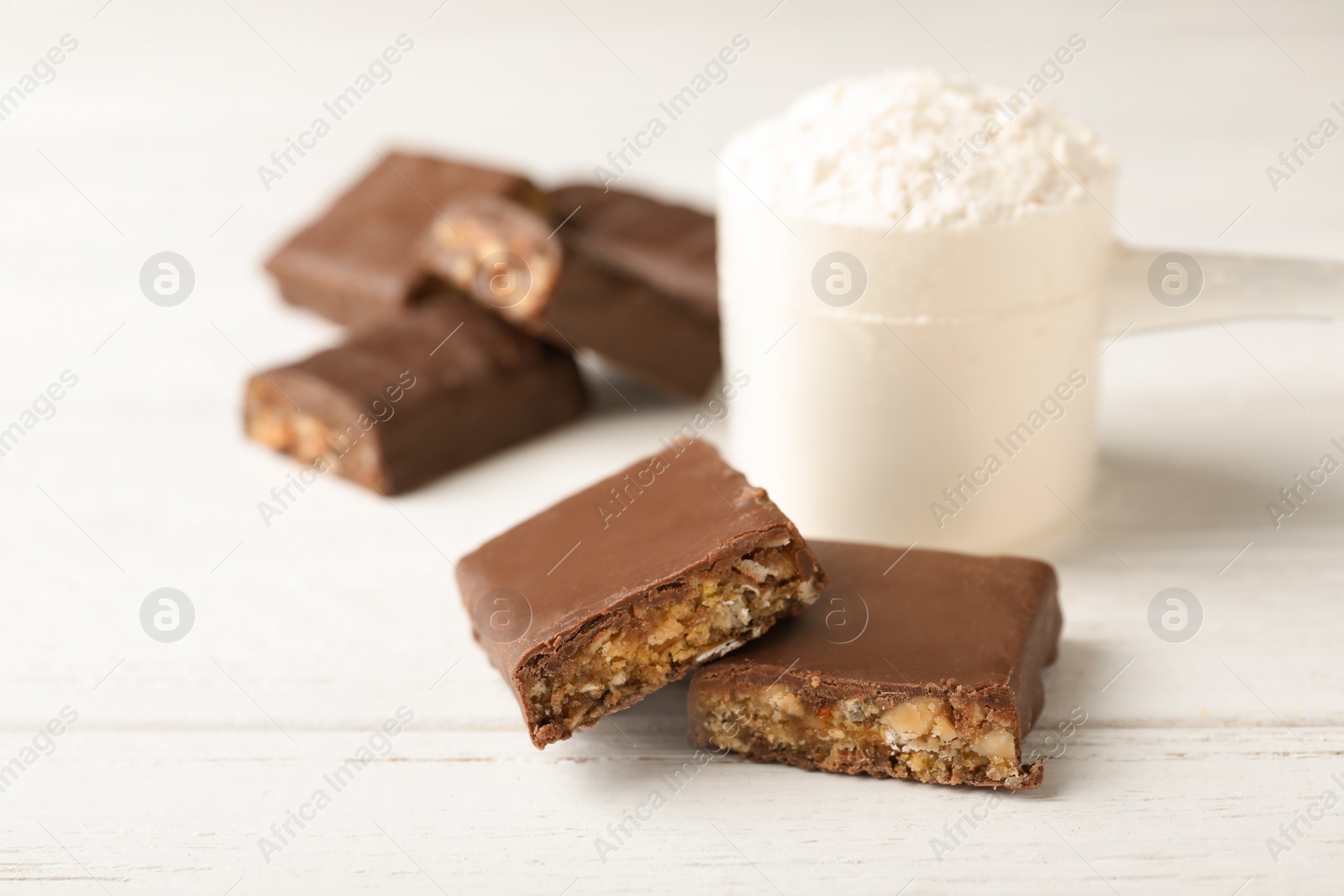 Photo of Tasty protein bars and scoop of powder on white table. Space for text