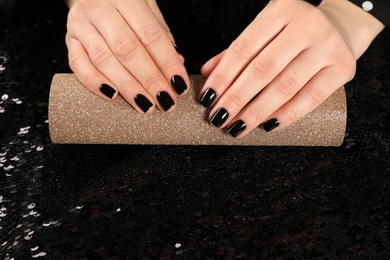 Photo of Woman showing black manicure on rolled shiny paper, closeup with space for text. Nail polish trends